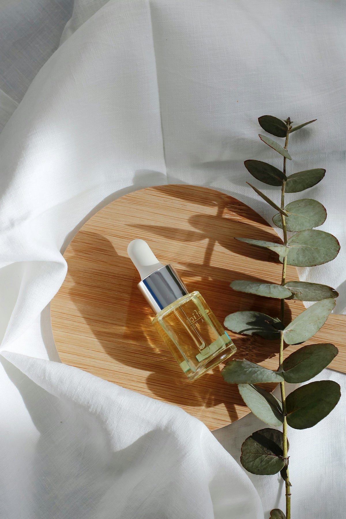 Dewdrop Hydrating Serum dropper bottle on a wooden tray with eucalyptus